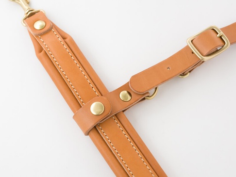 職人手作皮革背包用減壓胸前扣帶 (KO-2)，以淺棕色皮革製成，搭配黃銅色金屬扣件和鉚釘，縫線整齊，設計簡約。
