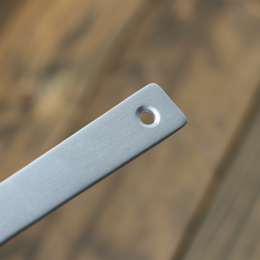 銀色鋁製湯勺的長柄，表面有細緻的拉絲紋理，末端有一個圓形掛孔。