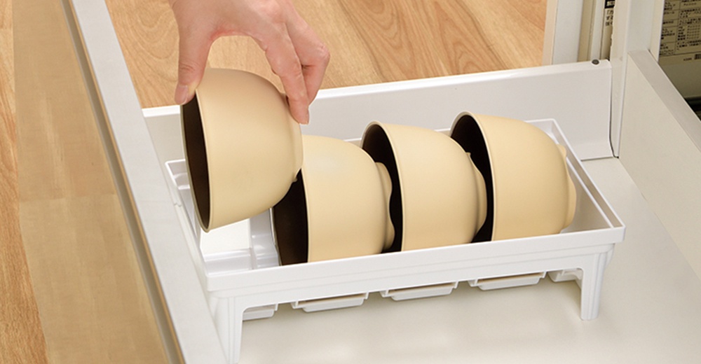 手正在將淺褐色碗放入白色抽屜式餐碗收納架中