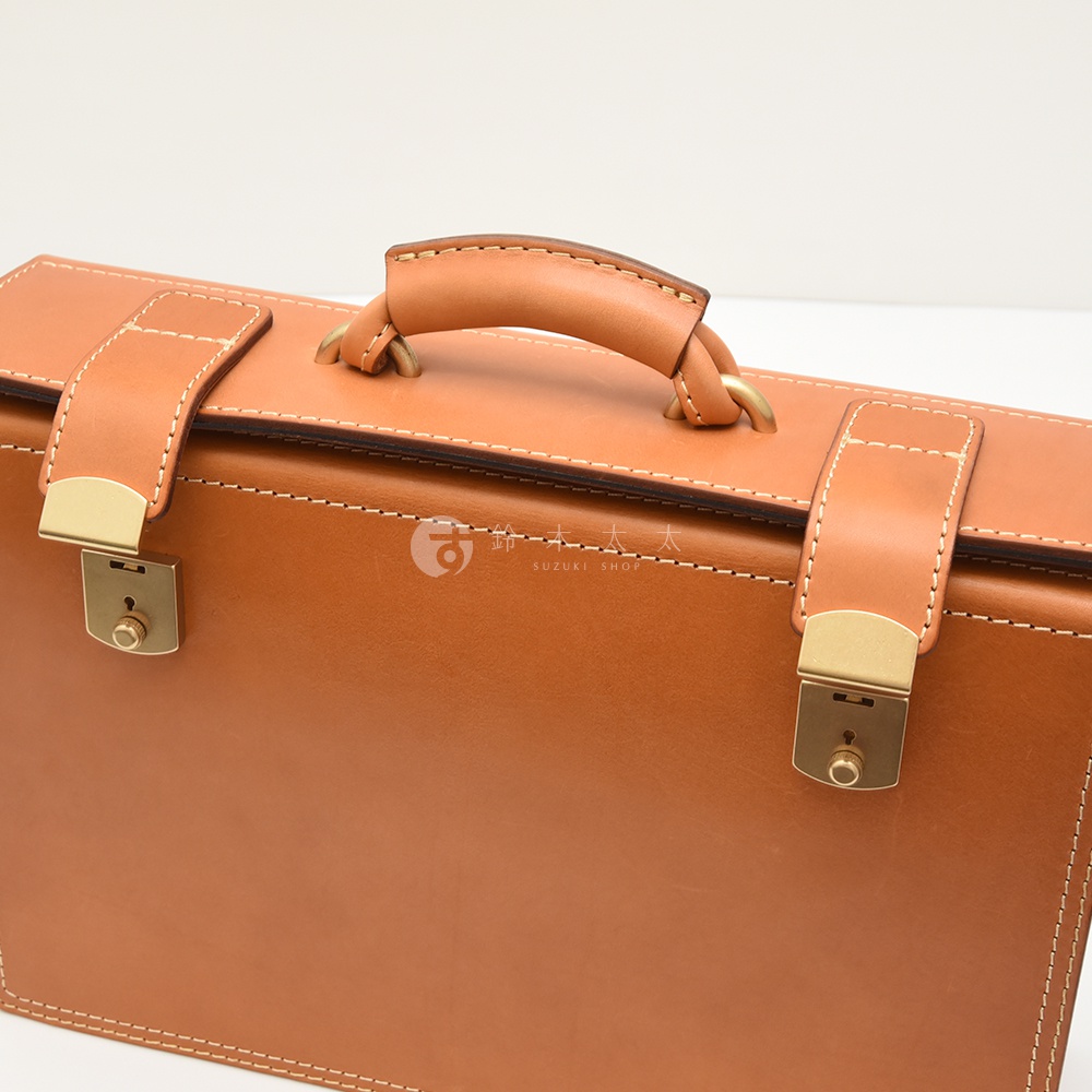職人手作皮革兩用機師箱，採用光滑的棕褐色皮革製成，搭配金色鎖扣和金屬環的提把，整體風格簡潔俐落。
