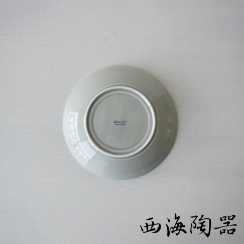 一個淺灰色、圓形、陶瓷材質的盤子，底部朝上，中央有藍色「Hasami Made in Japan」字樣。