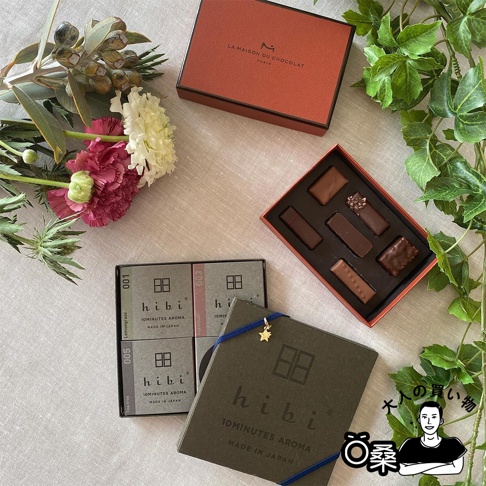香氛火柴禮盒，包含一盒巧克力、四盒香氛火柴及一束花。巧克力禮盒為橘紅色，內有六種不同造型的巧克力。香氛火柴禮盒為灰色，上面印有「hibi」字樣。