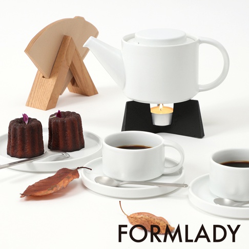 白色陶瓷茶壺，搭配黑色加熱座上的茶蠟，旁邊有兩個法式費南雪蛋糕、咖啡杯和濾紙架。