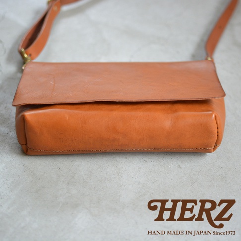 職人手作皮革Organ隨身斜背包 G-37，採用溫潤的棕褐色皮革製成，包身線條簡約，翻蓋設計，搭配同色系皮革背帶，整體散發著復古質感。包包底部有HERZ字樣的品牌標誌，下方並有HAND MADE IN JAPAN Since1973字樣。