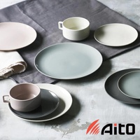 Aito 品牌旗下，一系列美濃燒簡約素雅質感的圓餐盤及杯具，以柔和的粉色、灰色和白色調呈現，擺放在灰色布料及水泥紋理的桌面上，營造出寧靜而優雅的用餐氛圍。