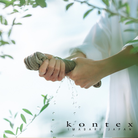 在柔和的自然光影下，一名穿著白色衣物的人手持一條灰褐色的 KONTEX 備長炭毛巾，雙手用力擰乾，晶瑩的水珠從毛巾中滴落。畫面底部印有 kontex IMABARI JAPAN 字樣，呈現出清新潔淨且高品質的品牌形象。