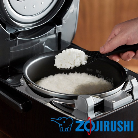 黑色壓力IH電子鍋，內鍋盛有煮熟的白米，一只手正用黑色飯勺盛起一勺米飯。