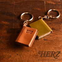 兩個皮革書本造型鑰匙圈，一個為棕色，印有「HERZ」及「MADE IN JAPAN」字樣；另一個為橄欖綠色。皆配有金色鑰匙圈。