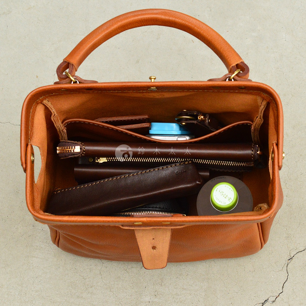 職人手作皮革Organ兩用方形口金托特包，呈現自然棕色調，主體為皮革材質，包內裝有手機、長夾、零錢包等物品，展現其收納機能。