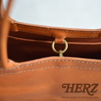 HERZ logo with text HAND MADE IN JAPAN Since1973 on a close-up view of a tan leather bag.