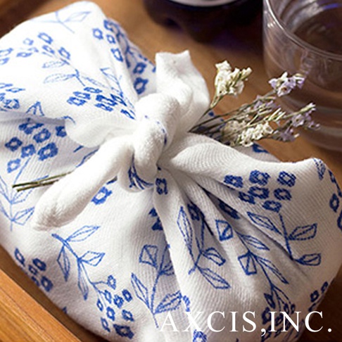 純棉花草紗布大拭巾，白色底布印有藍色花草圖案，巾身以白色紗布打結包裹物品，並點綴乾燥花束。