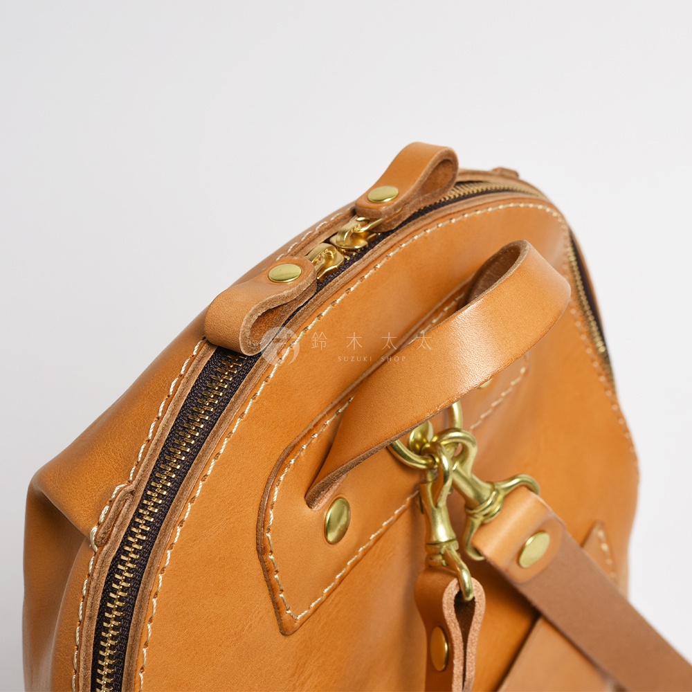 職人手作皮革大開口圓角後背包 R-18，展示焦糖色皮革，特寫拉鍊、皮革提把、銅製掛鉤與縫線細節。