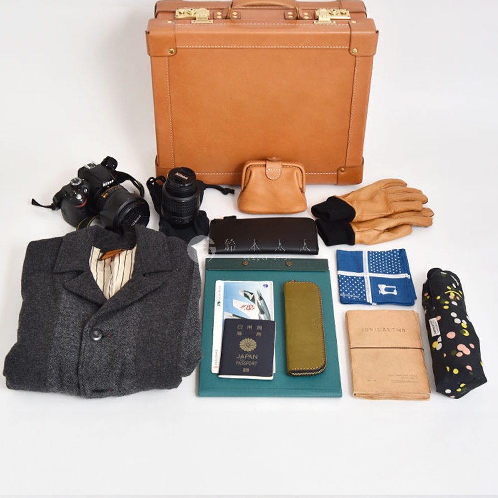 皮革手提行李箱，搭配相機、錢包、手套、外套、護照、筆記本及印花雨傘等配件。