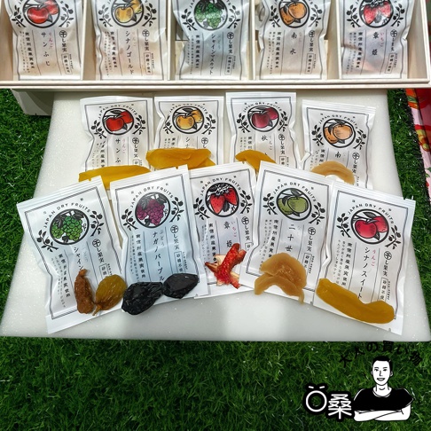 長野縣南信州果乾20入桐木禮盒，包含多種獨立包裝的各式果乾，如草莓、葡萄、水蜜桃、柿子等，包裝上印有水果圖案與日文說明，整體呈現豐富多樣的色彩。