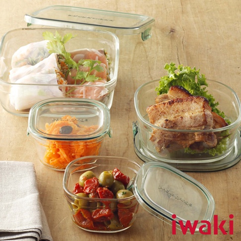 一套四個耐熱玻璃保鮮盒，其中三個裝有食物：一個裝有春捲和香草，一個裝有切絲胡蘿蔔，另一個裝有橄欖和番茄。一個較大的透明玻璃保鮮盒裝有豬肉塊和生菜，旁邊還有一個蓋子。