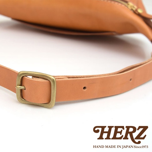 淺棕色皮革輕便斜背包，特寫其可調節的皮革背帶和復古黃銅色帶扣。