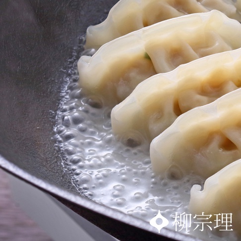 柳宗理雙網紋單手鐵鍋內正煎煮著數顆半透明且飽滿的日式煎餃，滾燙的油水在鍋底形成細密的泡沫，凸顯出鍋具獨特的紋理表面與煎餃誘人的金黃色澤。