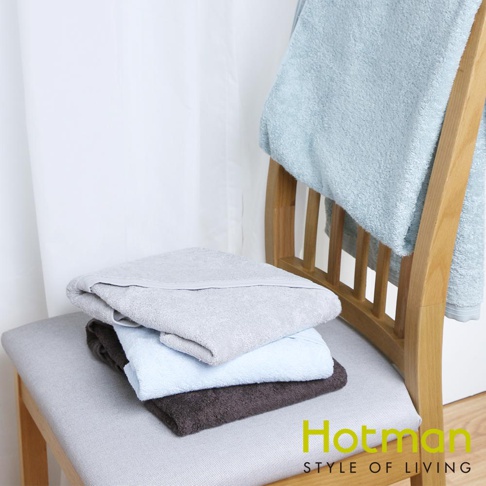 一疊三條毛巾，分別為淺灰色、淺藍色和深棕色，材質看起來為柔軟的棉質。另一條淺藍色毛巾掛在木椅的椅背上。