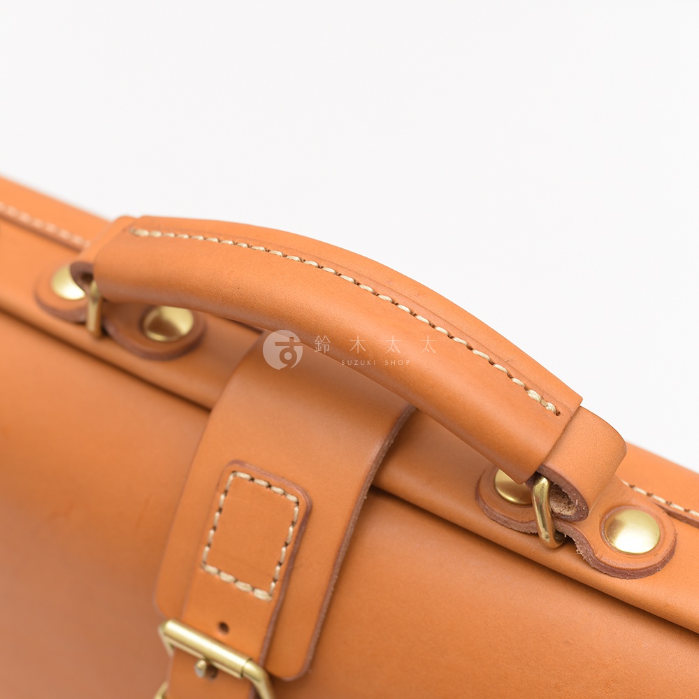職人手作皮革軟式杜勒斯包，特寫皮革提把及金屬扣件，展現自然皮革紋理與精緻車縫工藝。