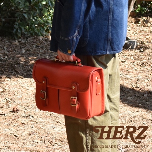 一個紅色皮革製成的兩用單肩包，具有頂部手柄、翻蓋和兩個金屬扣。