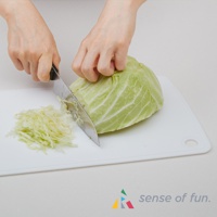 白色矽膠砧板上，一隻手正拿著刀，將綠色高麗菜切成絲狀，砧板上已有一堆切好的高麗菜絲。
