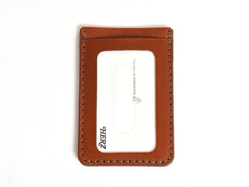 職人手作皮革直式票券收納夾，焦糖棕色，皮革材質，正面有透明窗口，窗口內印有「The Heart of Craftsmanship」字樣及小圖案，另有「HERZ」品牌標誌。