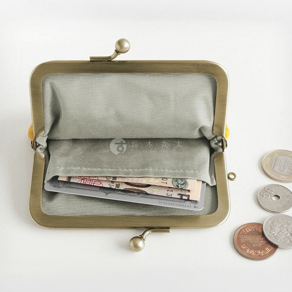一個打開的復古黃銅色口金包，裡面裝有日圓紙幣和卡片，旁邊散落著幾枚日本硬幣，包括 500 日圓、50 日圓和 10 日圓。