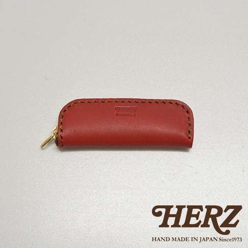 紅色皮革印章收納袋，拉鍊處有品牌標誌，手工縫線，材質為皮革。