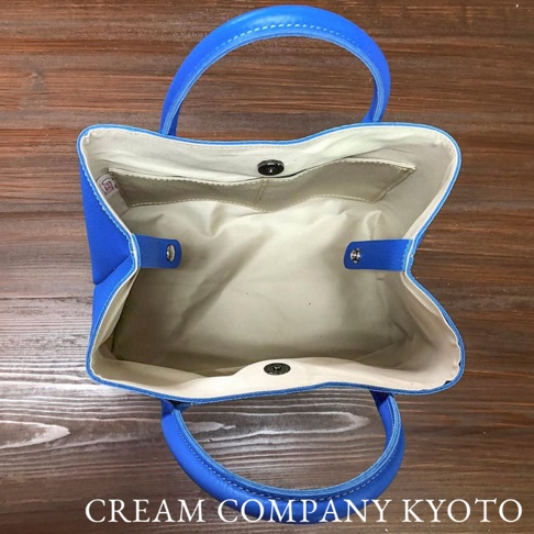 藍色皮革手提托特包，帆布內裡，內部有兩個開放式口袋和一個按鈕開合。