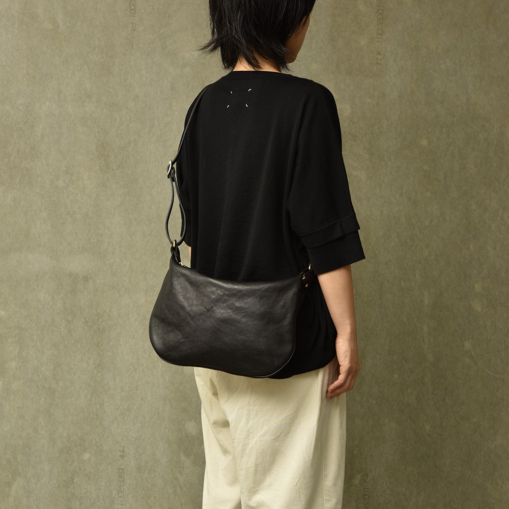 黑色皮革單肩半月包，以職人手作工藝製成，包身呈現自然皺褶，搭配可調節長度的肩帶，側邊有金屬扣環。