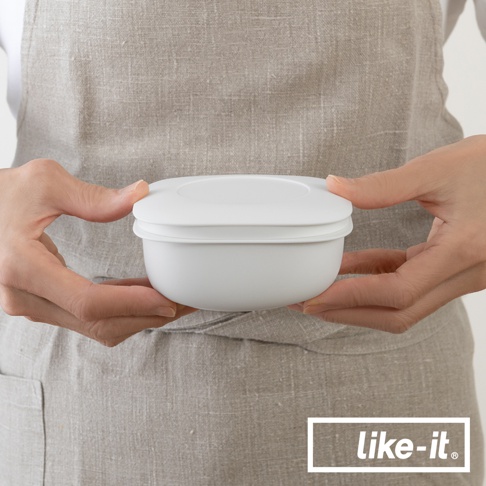 雙層白色保鮮盒，以雙手捧持，背景為亞麻材質圍裙，盒蓋與盒身結構清晰可見。