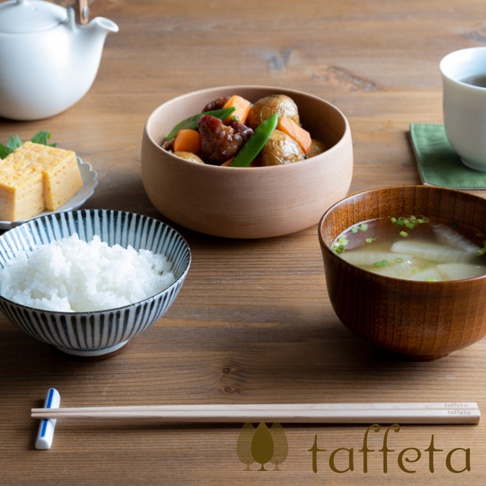 楓木沙拉碗，盛有燉煮的肉塊、馬鈴薯丁、胡蘿蔔塊和豌豆。旁邊是裝有白飯的藍白條紋碗，以及裝有味噌湯的木碗。