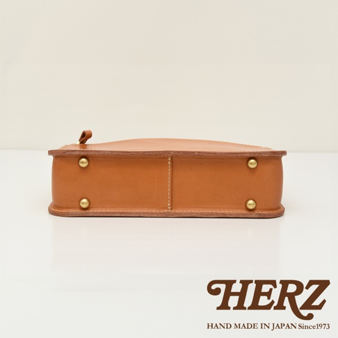 職人手作皮革兩用商務公事包，展示側邊，採用天然皮革材質，顏色為淺棕色，包身邊緣有縫線細節，並以黃銅色金屬鉚釘加固。