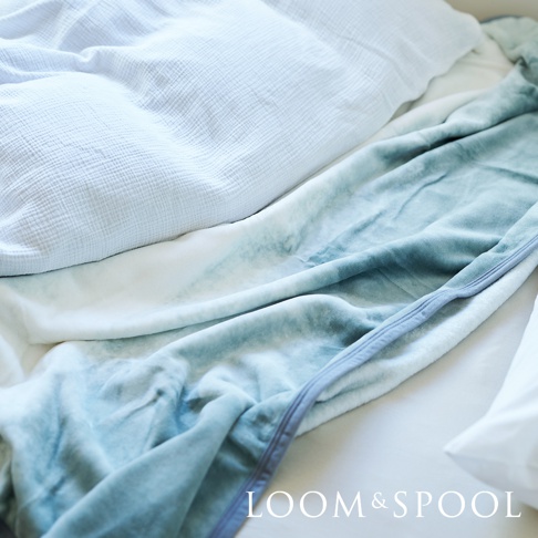 藍色與白色漸層的抗菌短絨舒柔雙人毯，鋪蓋在白色床單上，毯子觸感柔軟，邊緣有縫線裝飾。