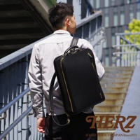 職人手作黑色皮革商務電腦後背包 R-25，搭配金色拉鍊，一個男性背著走在樓梯上。