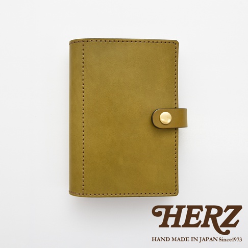 職人手作皮革手帳/記事本書套，採用黃褐色皮革製成，表面有一條皮革束帶及金色按扣，邊緣以細緻車縫線裝飾。