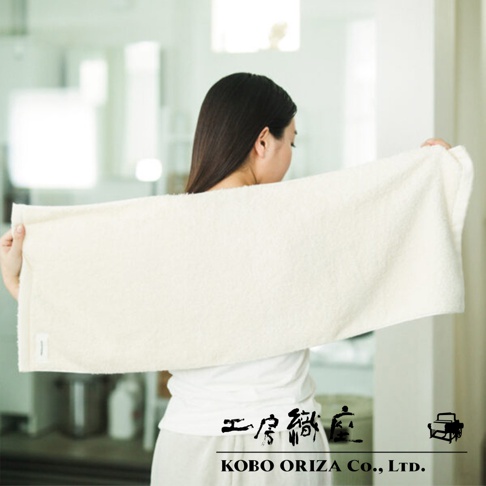 一名女子展示一條米白色超細纖維毛巾，毛巾材質柔軟，有高密度織紋。