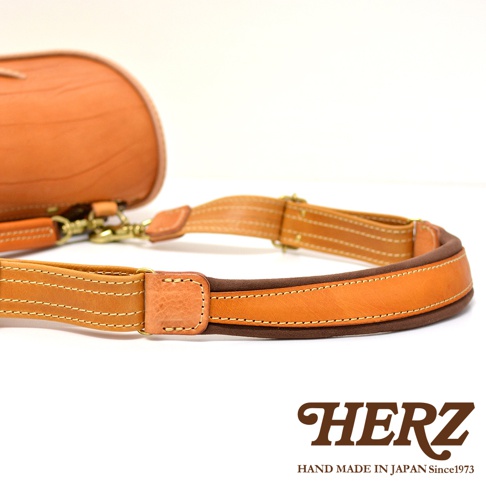 職人手作皮革郵差包，以棕色皮革製成，帶有鹿角扣細節。包款展現精緻縫線和金屬扣環，搭配可調節的皮革肩帶。