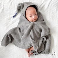 一名嬰兒被包裹在一件針織純棉的灰色連帽浴巾中，浴巾的帽子向上豎起，一條深藍色標籤從帽子一側垂下。