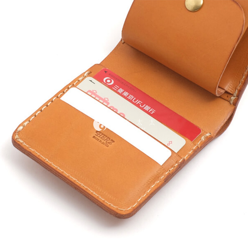 職人手作皮革原子釦型二折式短夾，展現自然原色皮革紋理，內有卡槽與鈔票夾層，搭配精緻車縫線與品牌烙印。