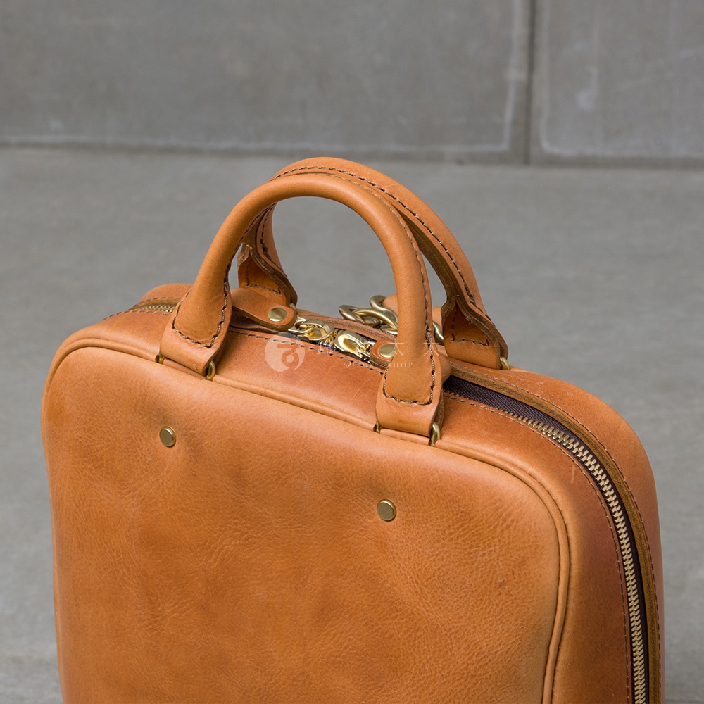 皮革後背包的頂部提把，細節處有拉鍊和金色金屬配件。