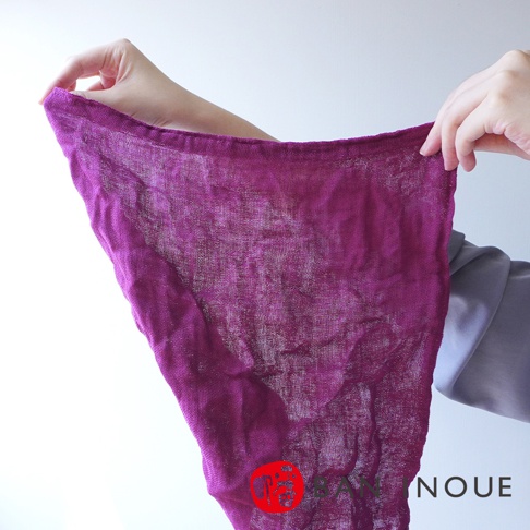 兩隻手拿著一塊紫色的三層蚊帳棉織迷你手拭巾，質地輕薄，織紋清晰可見。