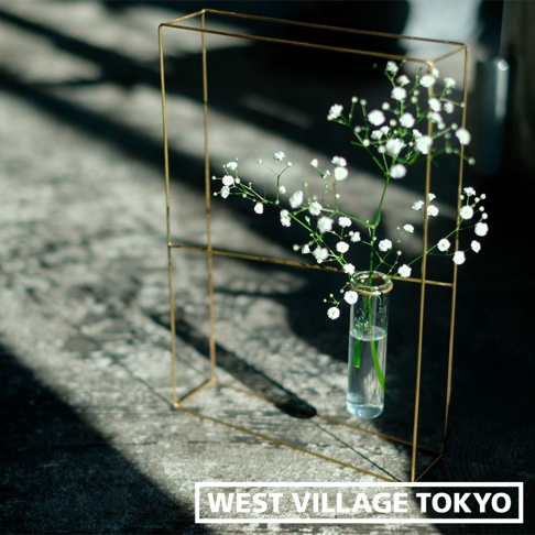 黃銅書本造型掛擺兩用花器，簡約的幾何線條框架，內置玻璃試管，插有白色滿天星，置於淺色紋理背景上，光影交錯。