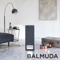 The Pure 空氣清淨機，機身為深灰色，造型為長方體，底部有白色發光面板，置於淺色大理石紋地板上，旁邊有復古風格的金屬行李箱和銅色飾品。