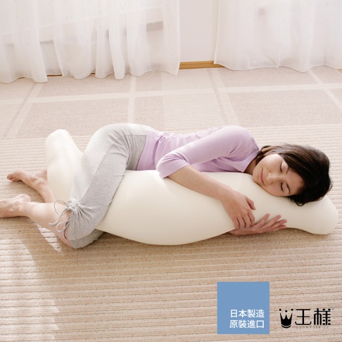 一名女性抱著一個米白色長條形抱枕，側臥在地毯上。抱枕呈彎曲狀，方便身體倚靠。