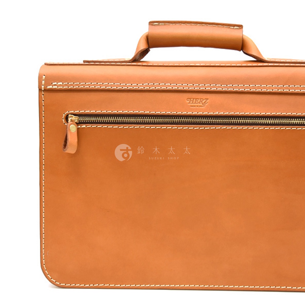 職人手作皮革經典雙扣兩用單肩包，採用棕褐色皮革，搭配白色縫線。包包有一個拉鍊開口，並印有品牌標誌。