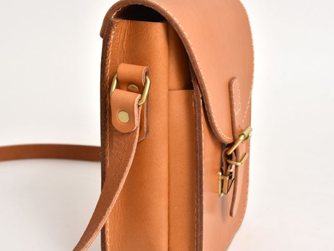 職人手作皮革翻蓋迷你單肩包，採用天然淺棕色皮革製成，附有黃銅色旋轉鎖扣和帶有鉚釘的金屬扣環，風格簡約。