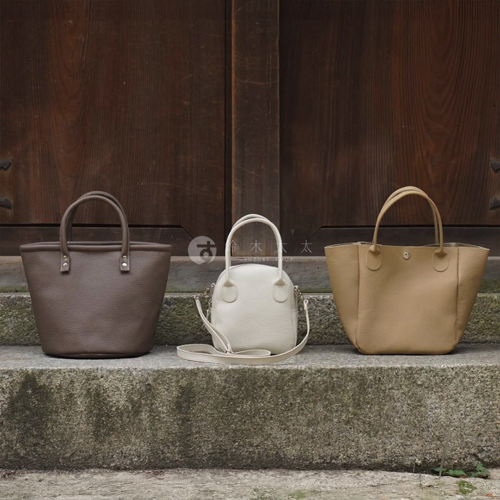 三款皮革手提包，分別為深棕色、米白色和淺棕色，皆為貝殼造型，配有手提帶和可拆卸肩帶。