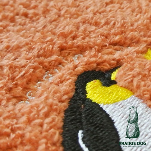 橘色精梳棉方巾，帶有企鵝刺繡圖案，材質柔軟。