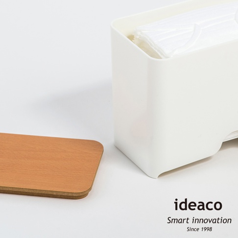 白色塑膠口罩收納抽取盒，內含疊放的白色口罩，旁邊擺放一個淺木色方形木蓋。